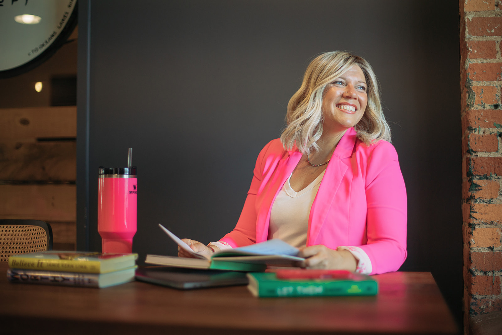 Jenn smiling at a table with her books and a pink tumbler